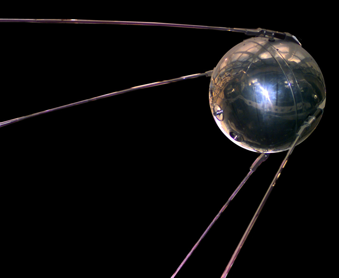 A polished replica of Sputnik 1 with its four antennas, on a black background
